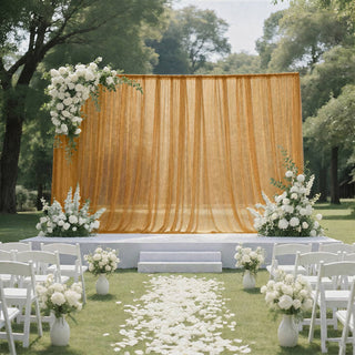 Outdoor wedding ceremony setup with gold drapery, white flowers, and chairs