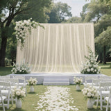 Elegant outdoor wedding ceremony setup with white flowers and draped backdrop
