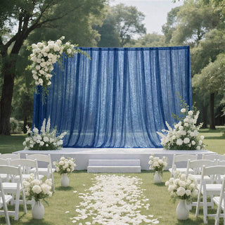 Outdoor wedding ceremony stage with blue drapes, white flowers, and chairs