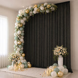 Elegant balloon arch with floral arrangements and candles on a black backdrop.