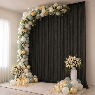 Elegant balloon arch with floral arrangements and candles on a black backdrop.