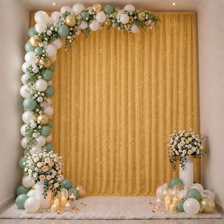 Elegant gold and sage balloon arch with floral decor and candles on a party backdrop