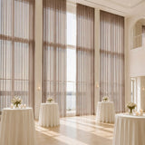 Elegant wedding reception with tall windows, sheer drapes, and floral cocktail tables