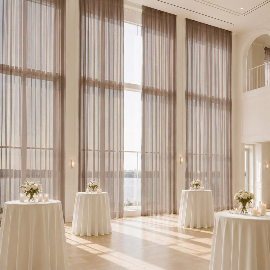 Elegant wedding reception with tall windows, sheer drapes, and floral cocktail tables
