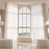 Elegant white wedding reception hall with tall arched windows and sheer drapes