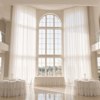 Elegant white wedding reception hall with tall arched windows and sheer drapes