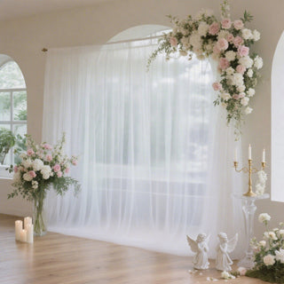 Elegant wedding backdrop with sheer white curtains and floral arrangements.