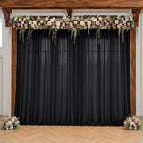 Wedding backdrop with black drapes, floral garland, and wooden frame