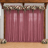Pink wedding backdrop with floral garland and sheer drapes under wooden beams