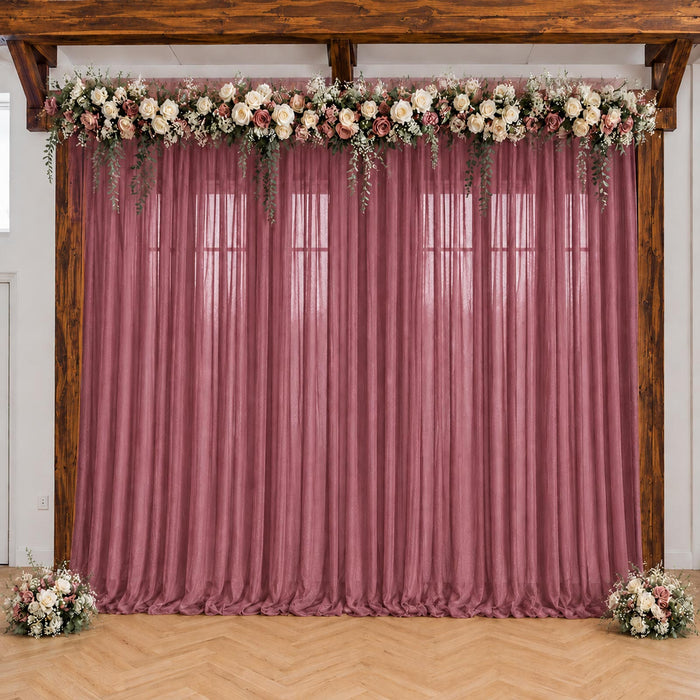 Pink wedding backdrop with floral garland and sheer drapes under wooden beams