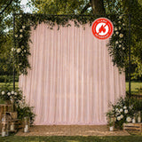 Outdoor wedding backdrop with blush drapes, greenery, and flame retardant sign