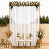 Elegant wedding backdrop with white drapery, gold chairs, and floral greenery