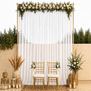 Elegant wedding backdrop with white drapes, gold chairs, and floral greenery