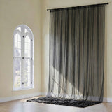 Sheer black curtain draped from a rod in a sunlit room with arched window.