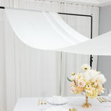 Elegant floral arrangement on a table with draped white fabric backdrop.