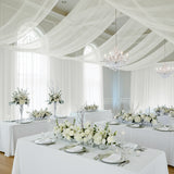 Elegant wedding reception with white floral arrangements and draped fabric decor.