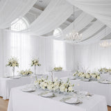 Elegant wedding reception with white floral arrangements and draped fabric decor.