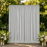 Outdoor wedding backdrop with white draped curtain and floral arrangements