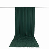 Dark green draped fabric curtain on a rod against a white background
