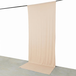Beige sheer backdrop curtain hanging from a black rod on a white wall