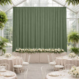 Elegant green backdrop in a decorated event space with floral arrangements and tables.