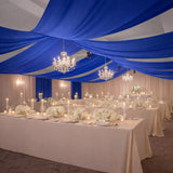 Elegant banquet hall with blue draped ceiling and floral centerpieces.