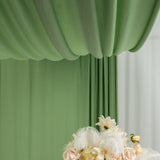 Green draped fabric backdrop with floral arrangement in front.