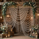 Elegant wedding backdrop with floral arrangements, string lights, and draped pearls.