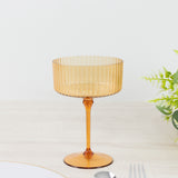 Amber ribbed glass cup on a light surface with greenery.