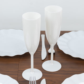 White plastic champagne flutes on a wooden table with white plates.