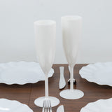 Two white champagne flutes on a wooden table with white plates.