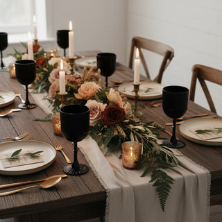 Elegant dining table set with black goblets, floral centerpiece, and candles.