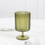 Green ribbed glass on a marble surface with utensils.