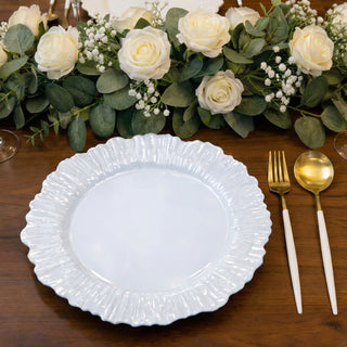 Elegant white ruffled plate with gold utensils beside floral arrangement.