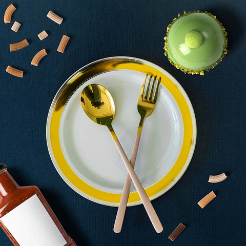 White plate with blue rim and gold flatware beside black napkin