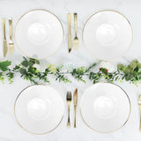 Elegant white plates with gold trim arranged with cutlery and greenery.