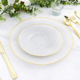Elegant clear plates with gold trim on a marble table setting.
