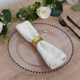Elegant white napkin with gold ring on a clear plate, surrounded by floral decor.
