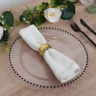 Elegant white napkin with gold ring on a clear plate, surrounded by floral decor.
