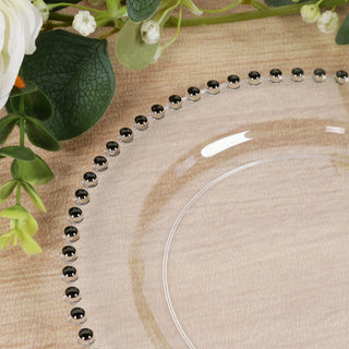 Clear glass plate with black beaded edge, surrounded by greenery and floral accents.