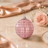 Pink mirrored disco ball ornament with rose floral decor on marble table