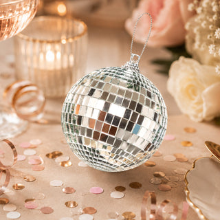 Silver disco ball ornament with champagne confetti and candles on a festive table