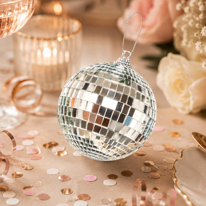 Silver disco ball ornament with champagne confetti and candles on a festive table