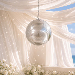 Silver disco ball hanging under sheer drapes with white floral decor and ocean view