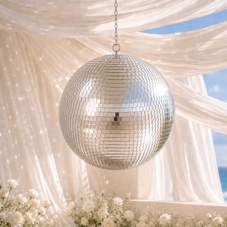 Silver disco ball hanging under draped fabric with white flowers and blue sky
