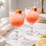 Two cocktails with cherries and citrus slices on a marble countertop.