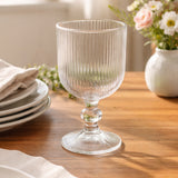 Clear ribbed glass goblet on a wooden table with floral decor.