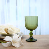 Green ribbed glass goblet on table with plates and white flowers