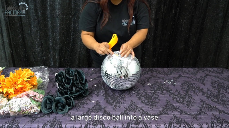 Person cutting into a silver disco ball to create a vase for a Halloween centerpiece.