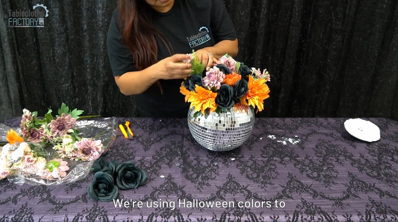 Person arranging Halloween flowers into a disco ball vase with black and orange blooms.